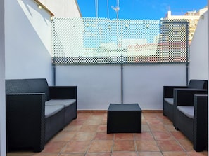 A patio with two wicker sofas and a small ottoman, a white wall, and a metal fence.