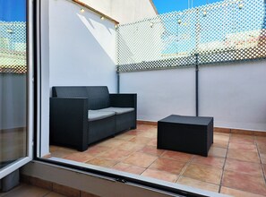 Ein Balkon mit einer schwarzen Rattan-Couch und einem kleinen schwarzen Hocker.