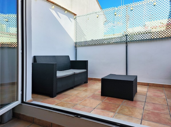 A balcony with a black wicker sofa and a small black ottoman.