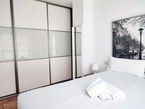 A hotel room with a bed, a large window with a view of a cityscape, and a wardrobe with frosted glass panels.