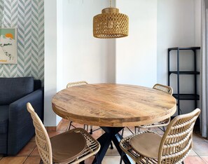 Ein runder Holzesstisch mit vier Korbstühlen, einer hängenden Lampenschirm aus Bändern und einem blauen Sofa im Hintergrund.