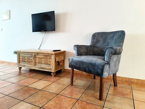A room with a television mounted on the wall, a wooden side table with a remote control, and a blue armchair.