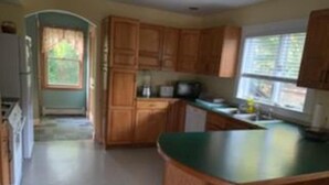 A kitchen with wooden cabinets, a green countertop, and a window providing natural light. - Oak Bluffs Rental - Walk to the Beach (Oak Bluffs)