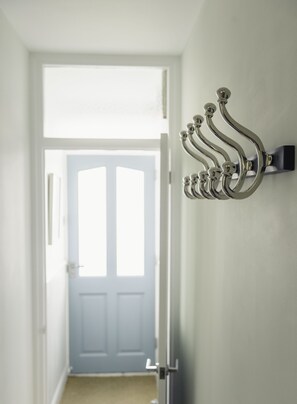 A hallway with a white door at the end, a wall-mounted metal hook, and a light-colored wall. - Stylish Coastal 3 Bed Haven | Close to town on Coronation Road (Salcombe)