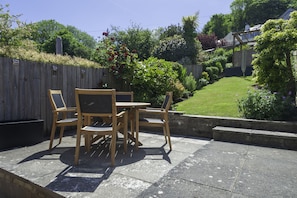 Une terrasse extérieure avec une table et des chaises en bois, entourée d’un jardin où poussent différentes plantes et délimitée par une clôture en bois.