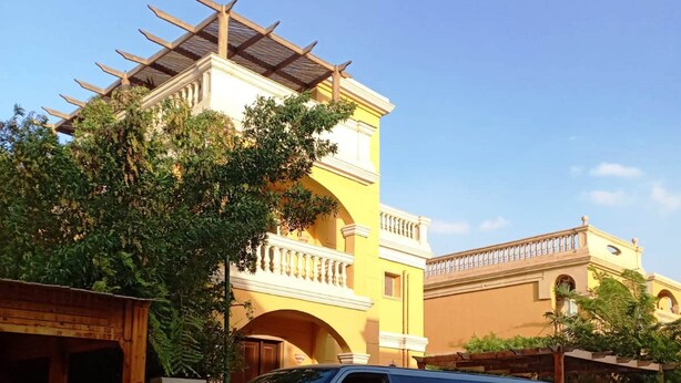 A silver car parked in front of a yellow building with a balcony and a pergola. - Stella villa (El Talaa City)