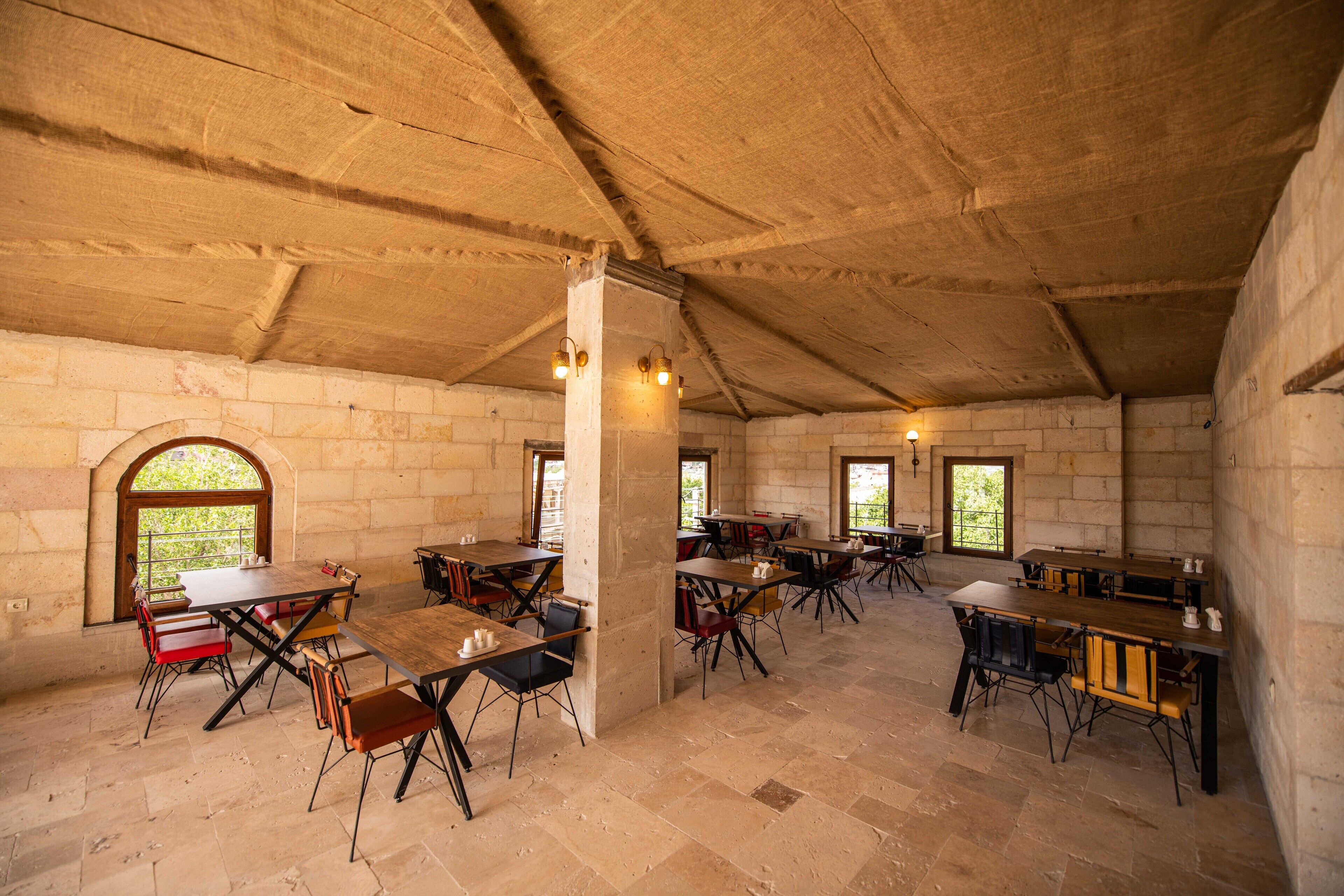 A spacious dining area with high ceilings and stone walls, featuring multiple tables and chairs arranged for dining.