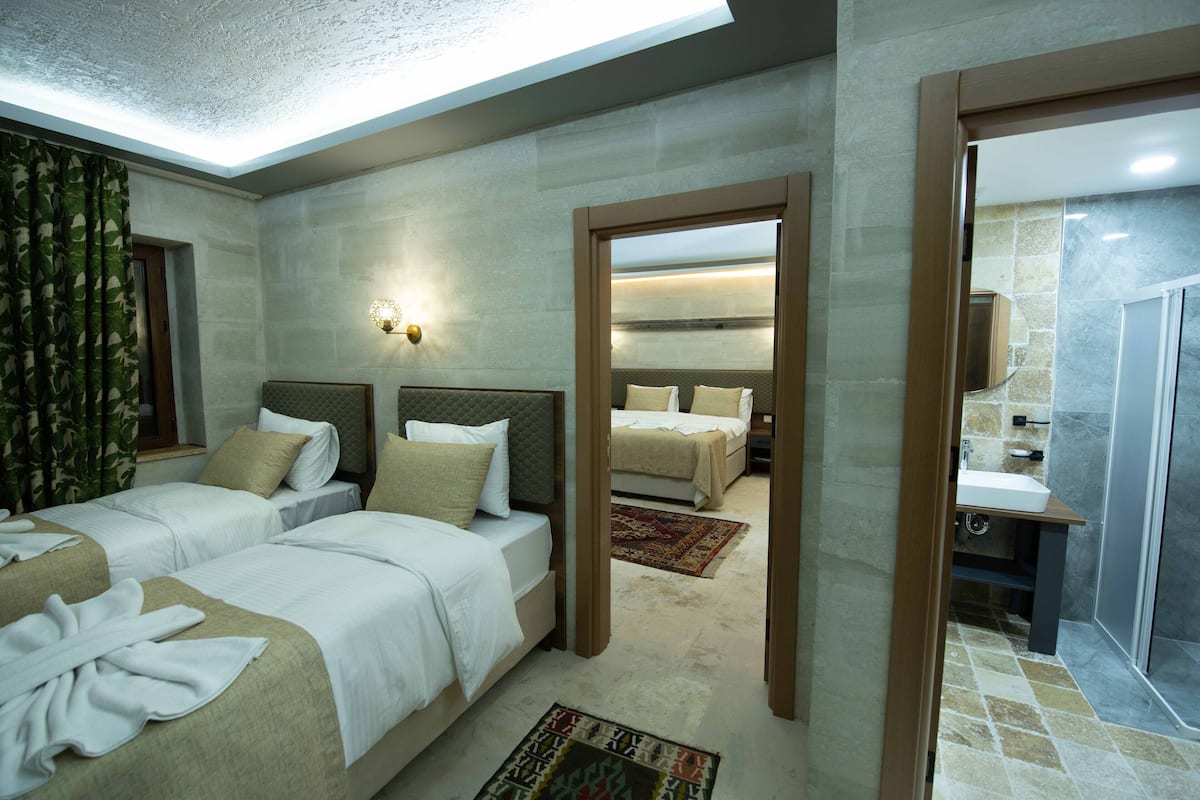 A hotel room with two beds, a skylight, a bathroom with a shower, and a mirror reflecting the room.