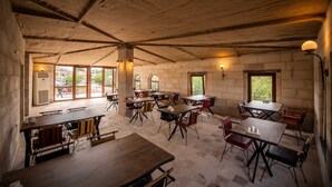 A rustic dining area with wooden tables and chairs, stone walls, and large windows allowing natural light. - Ahiyan Hotel (Nevsehir)