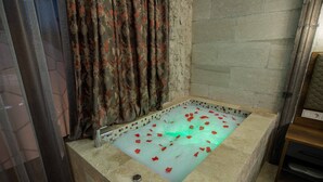 A bathtub with rose petals and a tiled floor. - Ahiyan Hotel (Nevsehir)