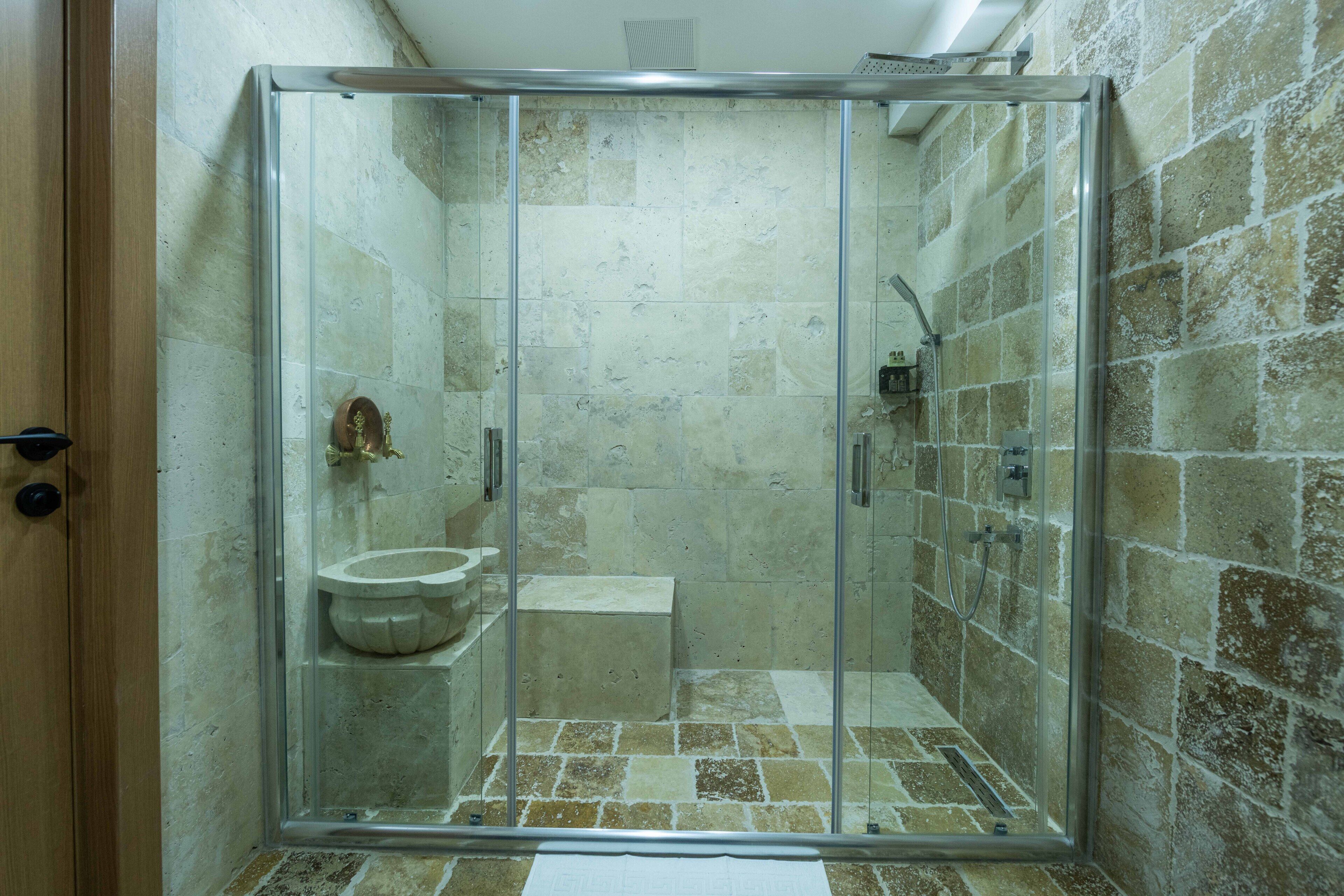 A glass-enclosed shower with a marble sink and a small step leading to a toilet.