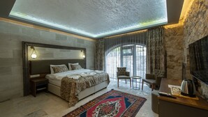 A bedroom with a large bed, a desk, a chair, and a fireplace. - Ahiyan Hotel (Nevsehir)
