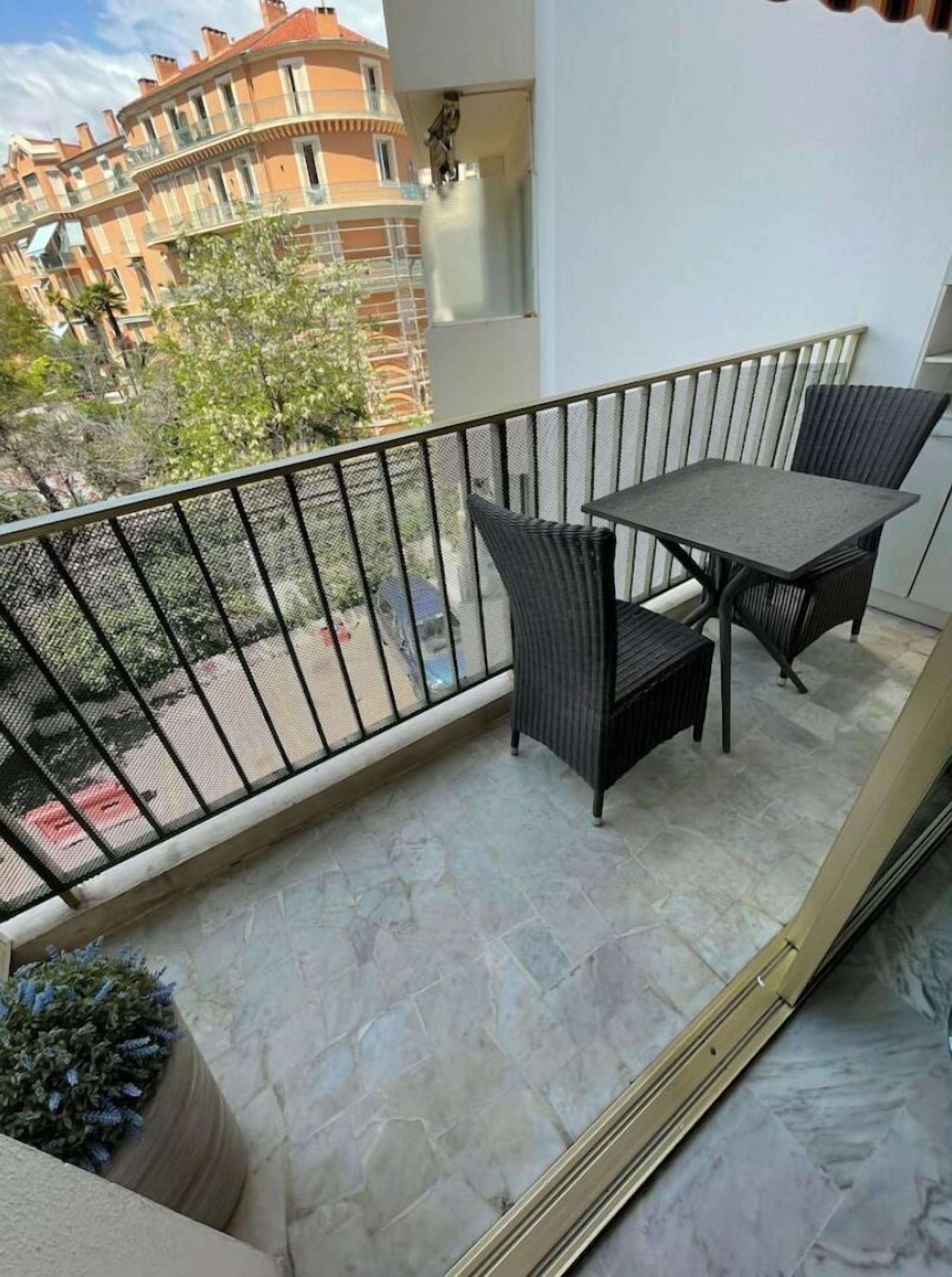 Un balcón con mesa y sillas, una planta en maceta y vistas a edificios en la distancia.