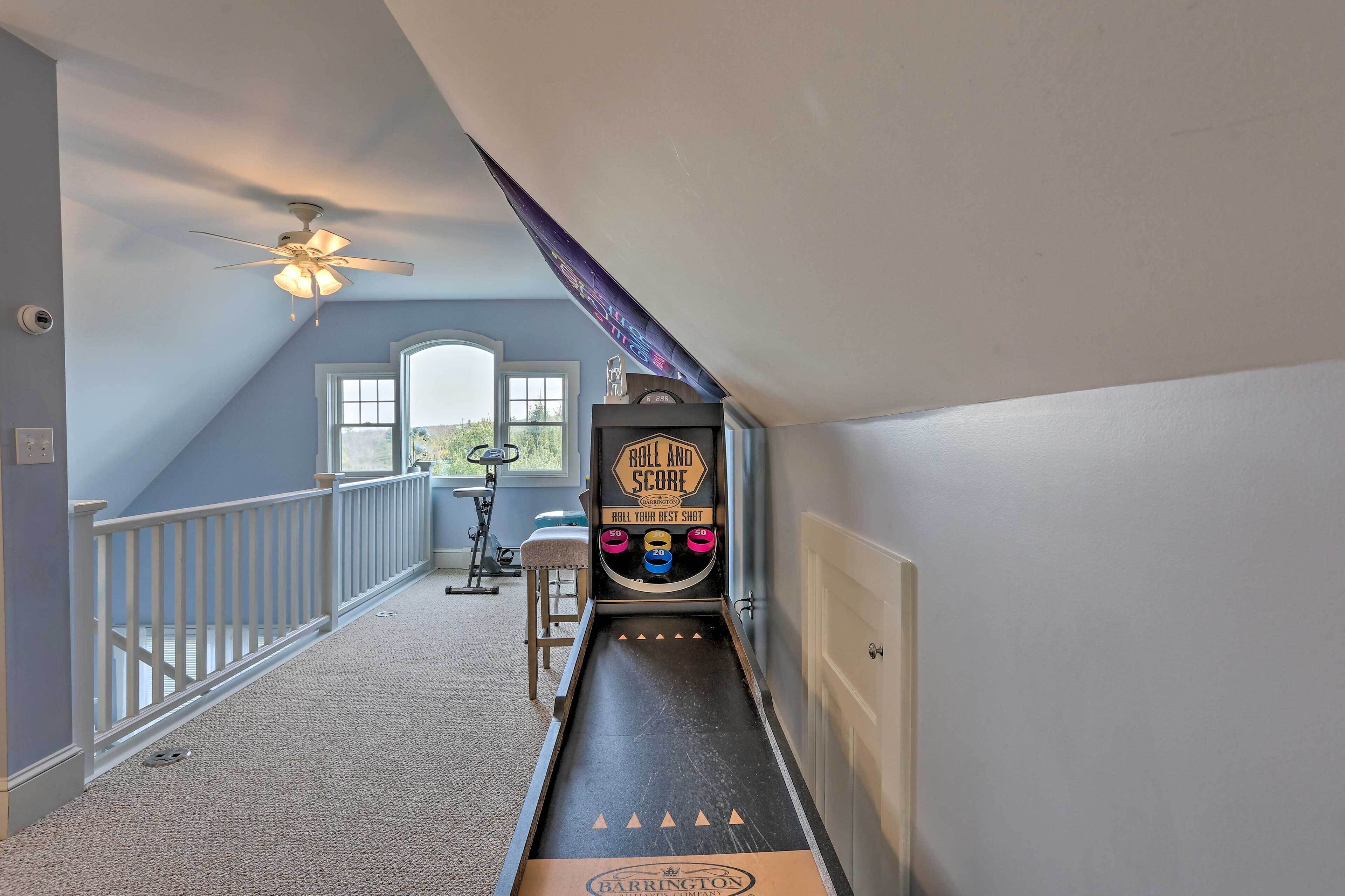 Un couloir étroit avec un flipper, un ventilateur de plafond et une fenêtre donnant sur un paysage verdoyant.