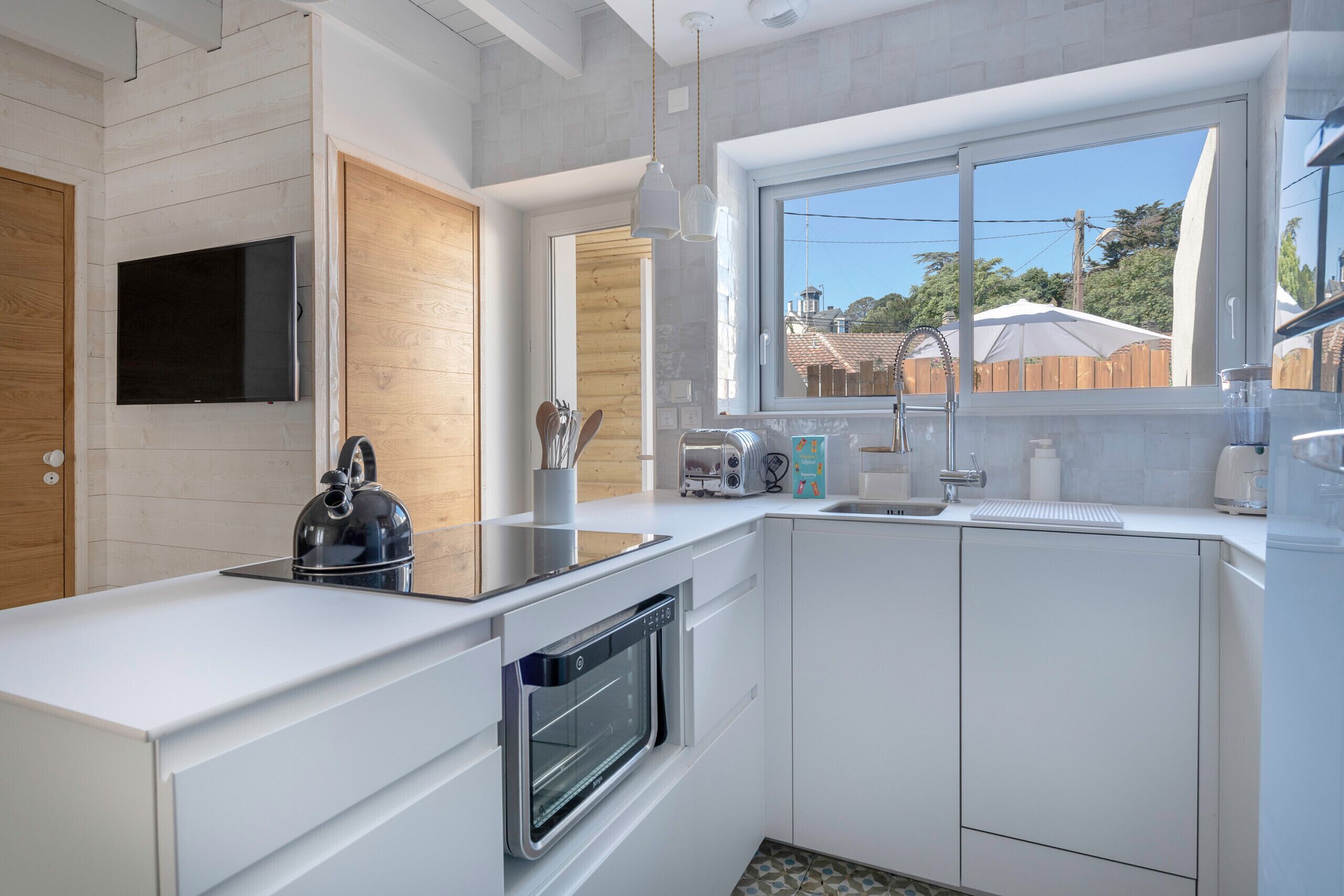 A modern kitchen with white cabinetry, a built-in oven, a kettle, and a window providing a view of the backyard.
