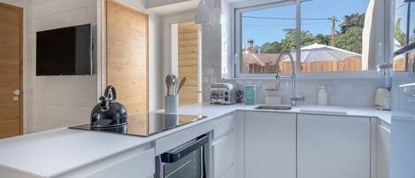 A modern kitchen with white cabinetry, a built-in oven, a kettle, and a window providing a view of the backyard.