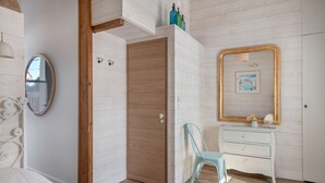 Ein Schlafzimmer mit Holztür, weißem Schminktisch, blauem Sessel und großem Spiegel mit goldener Rahmung.