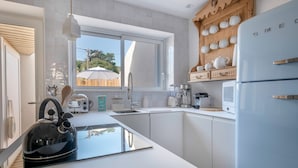 Eine moderne Küche mit weißen Schränken, einem schwarzen Wasserkocher und einem Holzregal mit weißen Tassen.