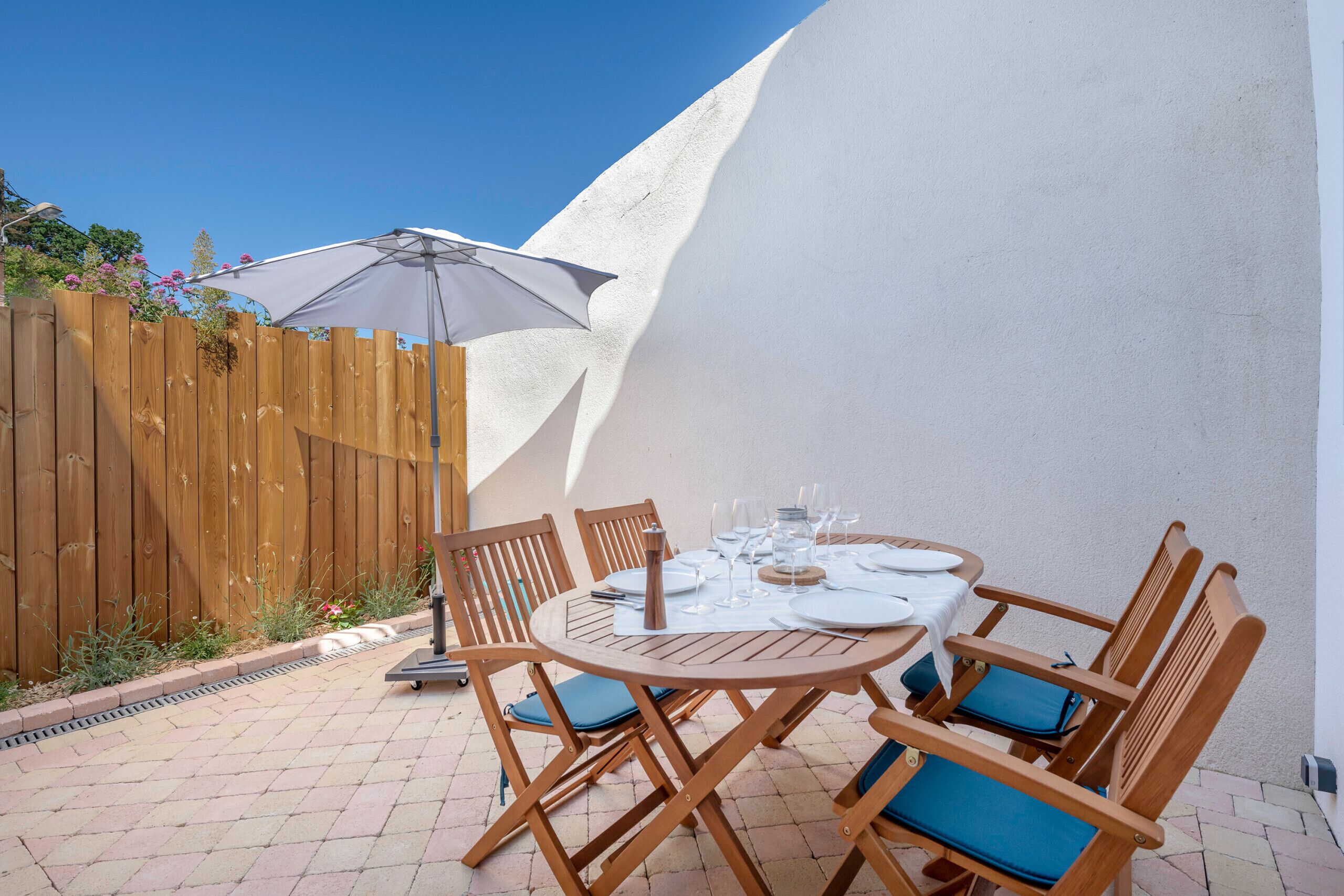 A round wooden table set with white tablecloth, blue cushions, and a white umbrella.