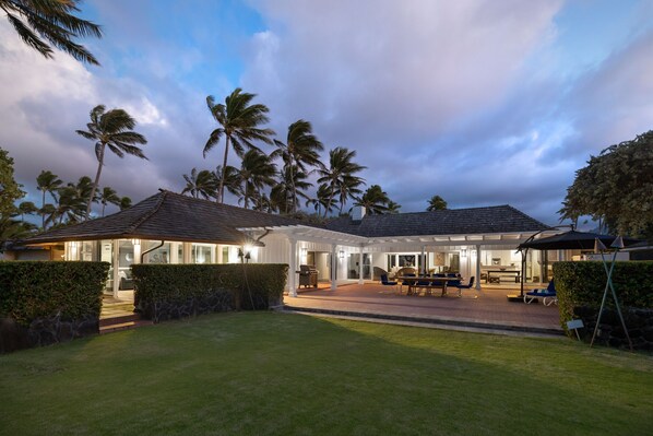 A house with a covered patio, a lawn, and palm trees.