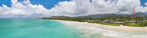 Ein Küstenort mit Strand, klarem türkisblauem Wasser und einer Bergkulisse im Hintergrund.