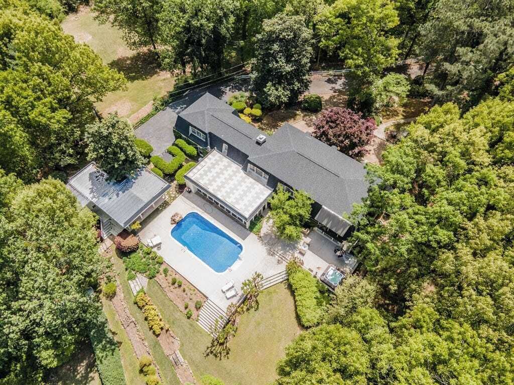Vista aérea de uma casa com piscina, rodeada por vegetação exuberante e árvores.