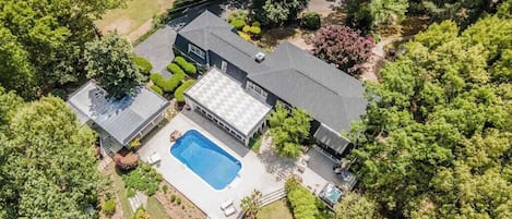 An aerial view of a house with a swimming pool, surrounded by lush greenery and trees.
