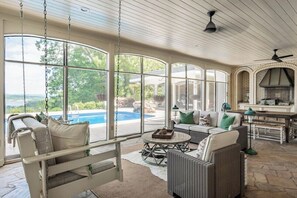 A sunroom with a view of a swimming pool, a sofa, a dining table, and a fireplace.