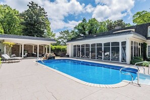 A swimming pool with a covered area, lounge chairs, and a stone patio.