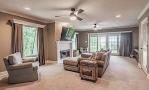 A living room with a fireplace, ceiling fans, and a large window. - Spacious 5BR estate with Jacuzzi, pool, patio, and full kitchen. (Guntersville)