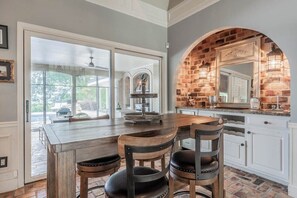 A kitchen with a brick archway, a dining table with chairs, and a large window.