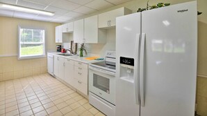 A kitchen with white appliances, including a refrigerator, oven, and microwave. There is a window with blinds, a sink, and a countertop with a kettle and a plant. - Waterfront Welaka Escape w/ Private Docks! (Welaka)