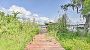 A wooden pathway leading to a small building by a body of water, surrounded by tall grass and trees. - Waterfront Welaka Escape w/ Private Docks! (Welaka)