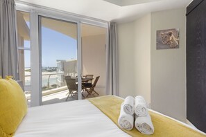 A hotel room with a bed, a yellow towel, a painting of a lion, and a balcony with a table and chairs.