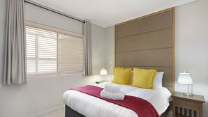 Une chambre d’hôtel moderne avec un grand lit, deux lampes de chevet et une tête de lit en bois.