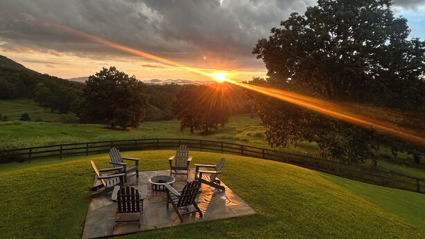 Eine Terrasse mit Adirondack-Stühlen und einer Feuerstelle, umgeben von einem Holzzaun und üppiger Bepflanzung.