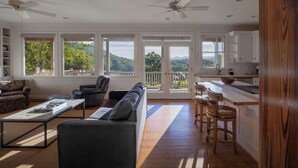 Ein großzügiger Wohnraum mit einer Couch, Sesseln und einem Couchtisch. Große Fenster bieten Blick auf Grünflächen und Berge.