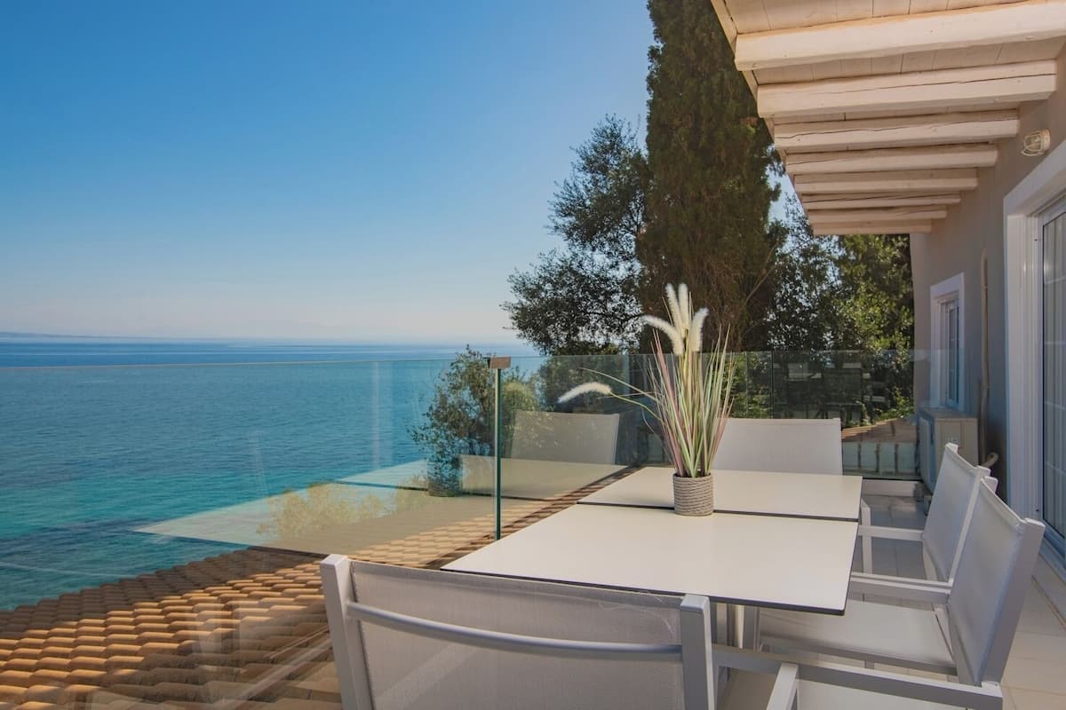 A terrace with a white table and chairs, overlooking a clear blue sea.
