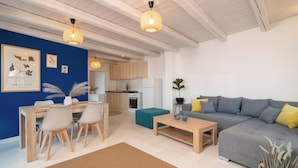 Ein modernes Wohnzimmer mit grauem Sofa, Couchtisch aus Holz und einem Essbereich mit Holztisch und Stühlen.