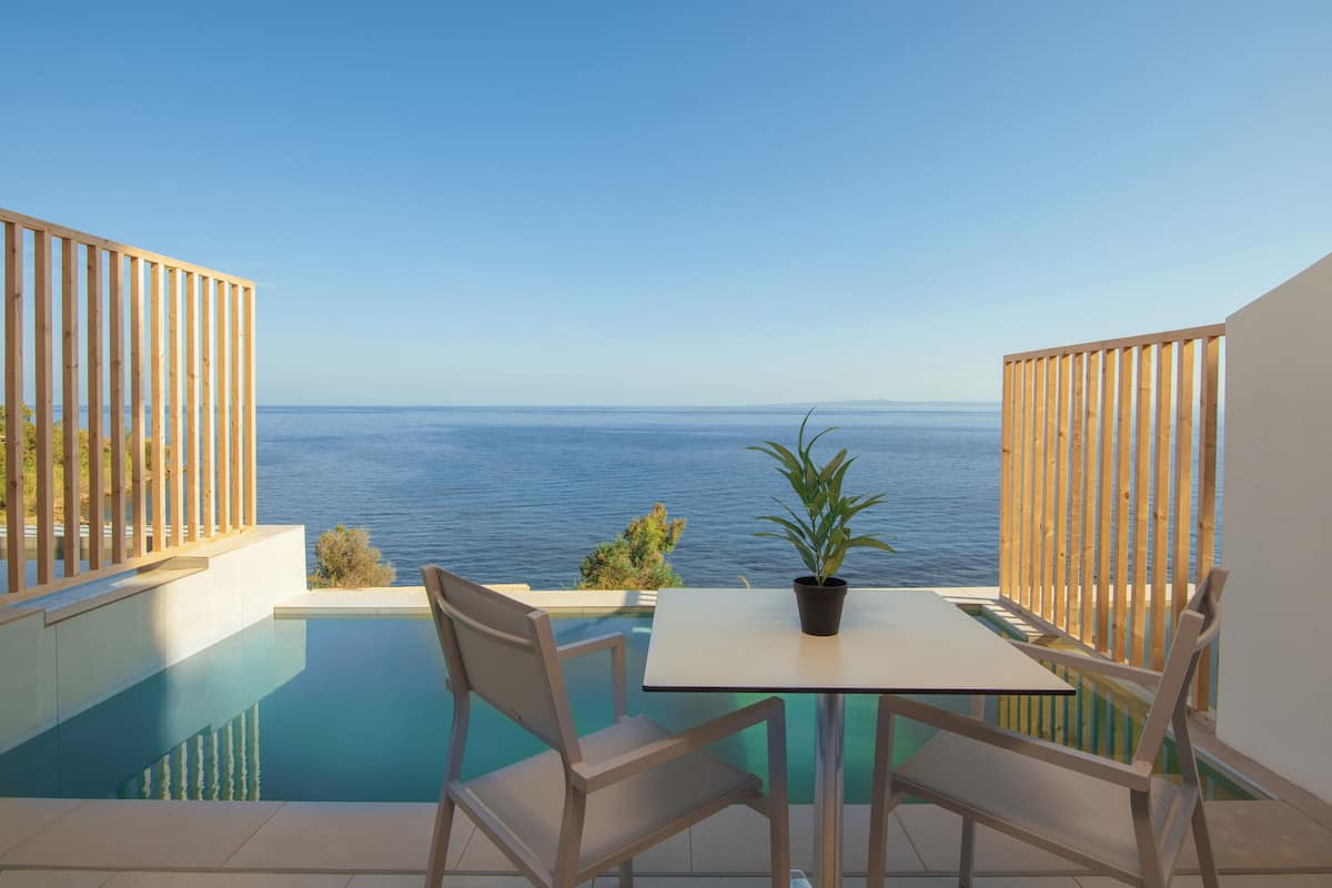 An infinity pool with a view of the sea, a table, two chairs, and a potted plant.