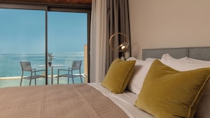 Ein Schlafzimmer mit einem großen Bett, zwei grünen Kissen, einem grauen Kopfteil und Blick auf den Ozean durch eine Schiebetür.