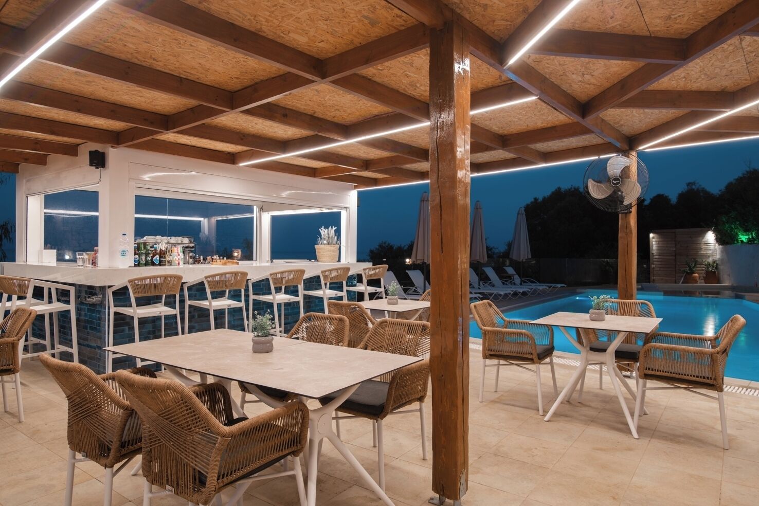 An outdoor dining area with wicker chairs and tables, a pool, and a bar with a view of the pool.