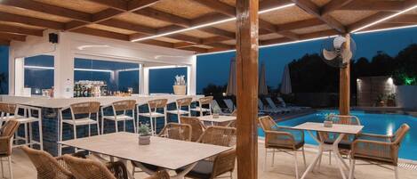 An outdoor dining area with wicker chairs and tables, a pool, and a bar with a view of the pool.