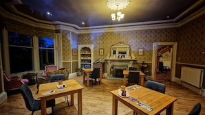 A dining room with wooden tables and chairs, a fireplace, and a chandelier. - The Pines Guesthouse (Elgin)
