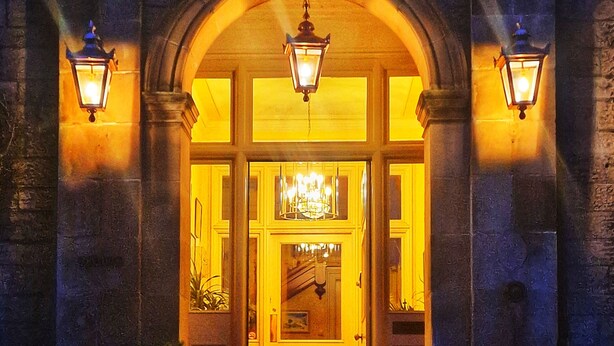 A grand entrance with a large arched doorway, illuminated by wall-mounted lamps and a central chandelier. - The Pines Guesthouse (Elgin)