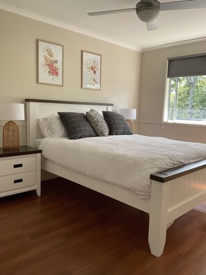 Une chambre à coucher avec un lit blanc, un parquet en bois foncé, deux lampes fixées au mur et deux œuvres d’art encadrées.