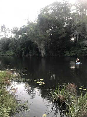 Une rivière paisible, bordée d’une végétation luxuriante, et une personne qui rame sur un radeau bleu.