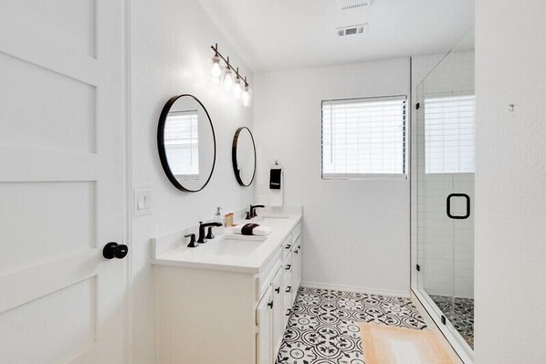 Une salle de bain moderne avec un meuble-lavabo blanc, deux miroirs et un espace douche.