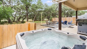 A hot tub with a wooden deck and outdoor furniture, surrounded by trees. - Woodacre Cottage I   Minutes to Jacob's Well (Wimberley)
