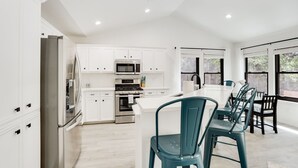 A modern kitchen with white cabinetry, stainless steel appliances, and a central island with teal chairs. - Woodacre Cottage I   Minutes to Jacob's Well (Wimberley)